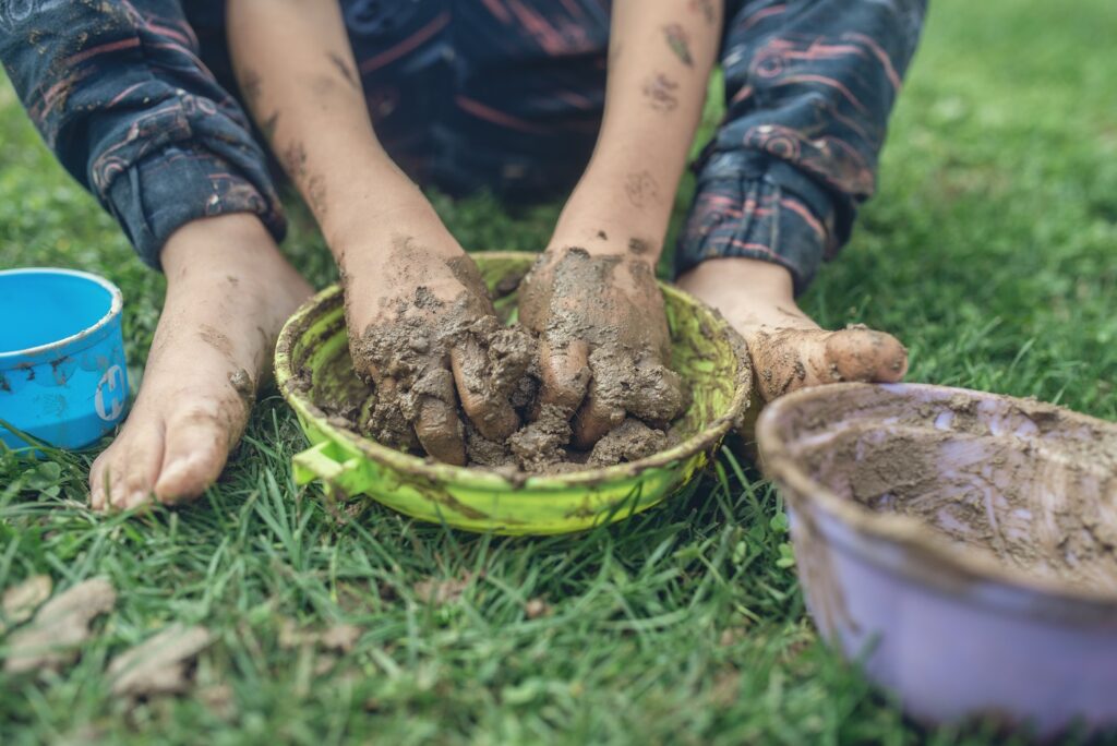 childs hands squishing mud in a bowl in grass