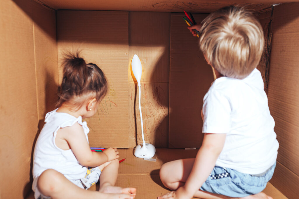 Two white toddler children playing and colouring in a large box