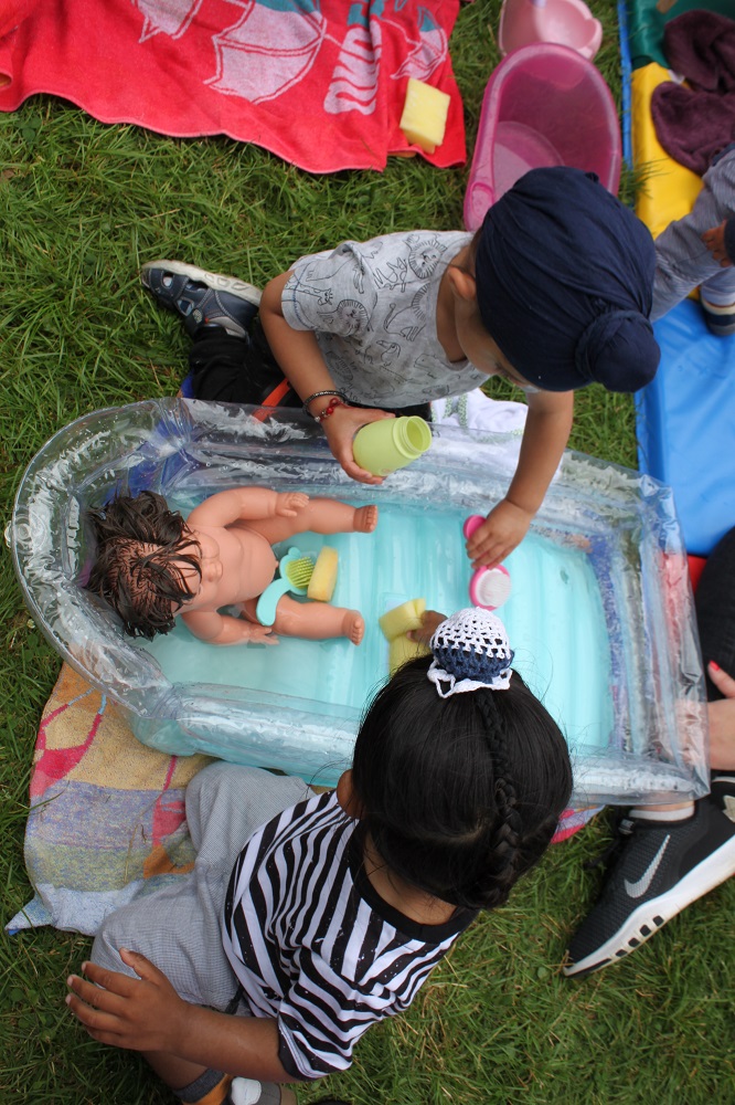 Two Asian boys washing a baby doll in a paddling pool