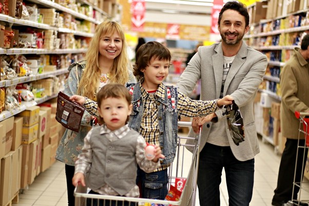 White family with two young sons in supermarket aisle. Both sons in the trolley