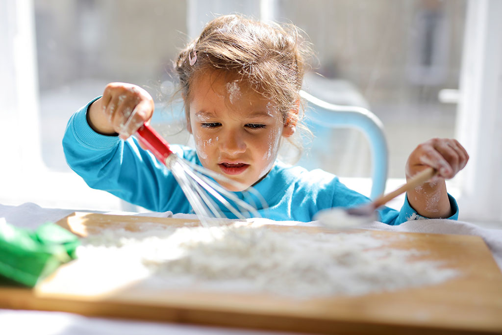 White appearing toddler girl playing with whisk in flour