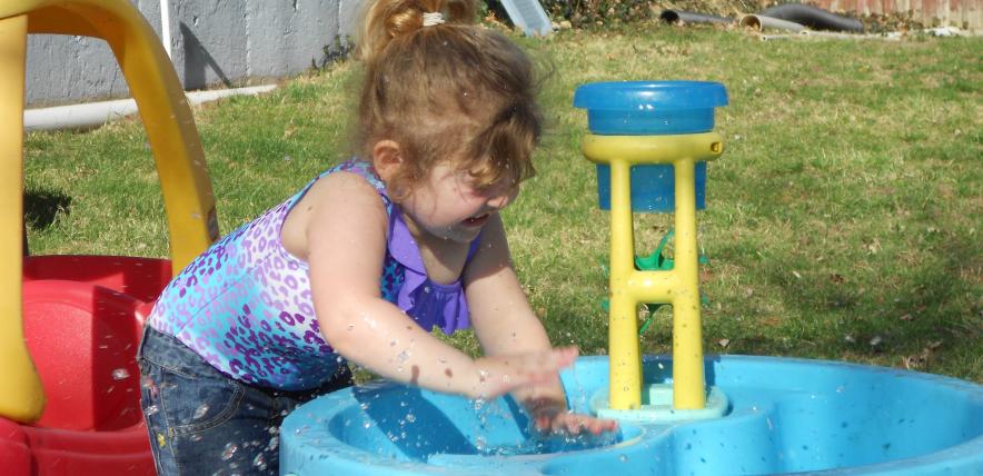 White toddler girl splashing hands in a paddling pool