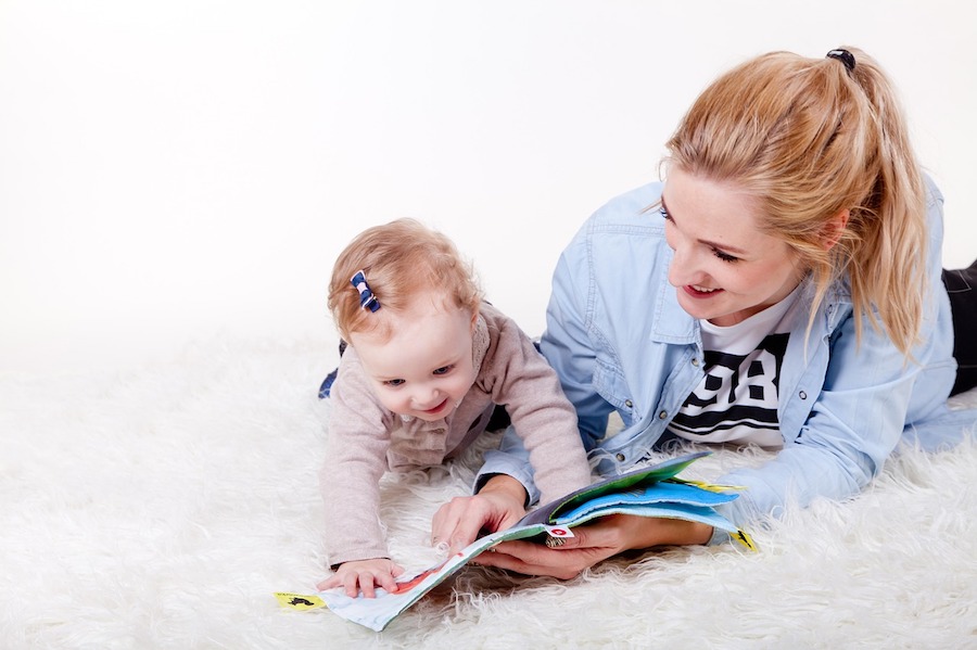 White blonde mother and her child laying down and reading a book smiling